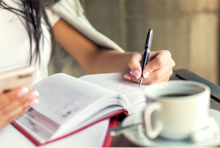 Woman practices writing in her journal with coffee nearby.